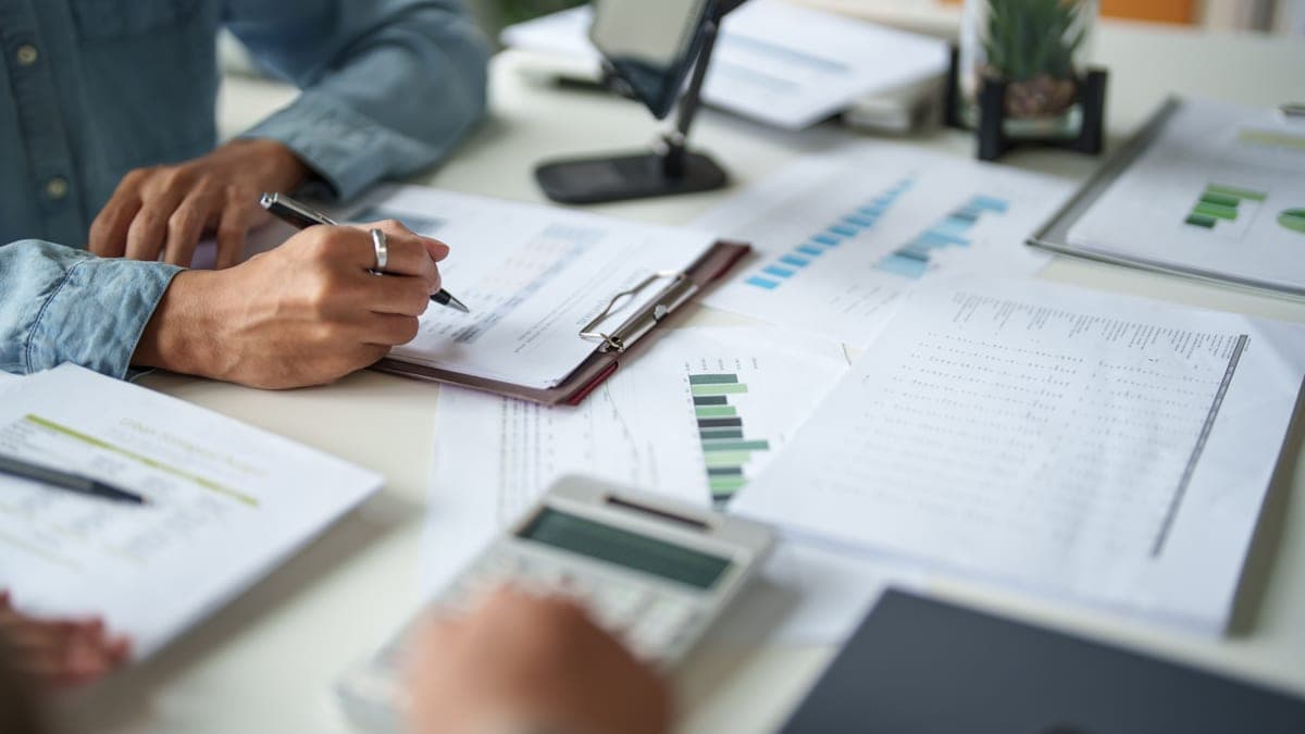 Unternehmer analysiert Finanzunterlagen, Diagramme und Kennzahlen mit Taschenrechner am Schreibtisch