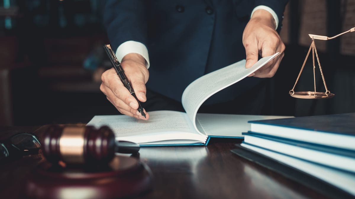 Jurist blättert in einem Vertragsdokument am Schreibtisch, daneben Richterhammer und Waage