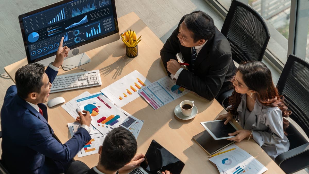 Besprechungstisch von oben: Team analysiert Diagramme auf Monitor und ausgedruckten Berichten